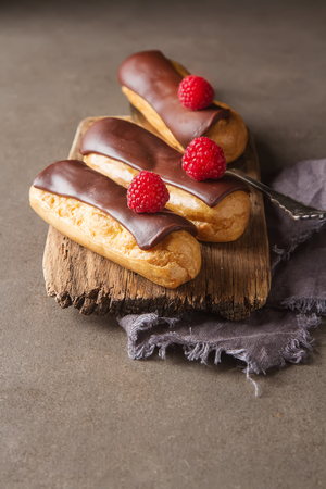 Traditional French dessert. Eclair with chocolate icing and raspberries. Dark backgroundの写真素材