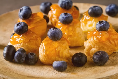 French traditional dessert. Profiteroles with blueberry and apricot jam. Dark background
