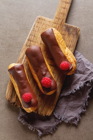 Traditional French dessert. Eclair with chocolate icing and raspberries. Dark backgroundの写真素材