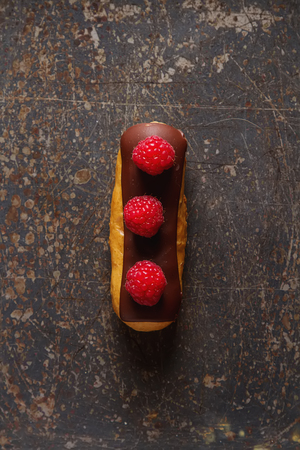 Traditional French dessert. Eclair with chocolate icing and raspberries. Dark backgroundの写真素材