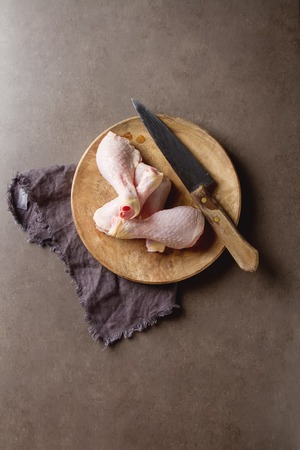 Chicken legs with a knife on a wooden board, napkin. Grey background. Lunch on the grill. Space for textの写真素材