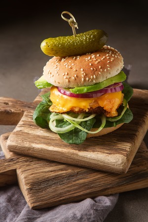 Fast food. Vegetarian burger with a chop, cucumber, tomato and lettuce. Tasty sandwich for lunch. Dark backgroundの写真素材