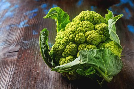 Ripe green cauliflower with leaves. Dark wood backgroundの写真素材