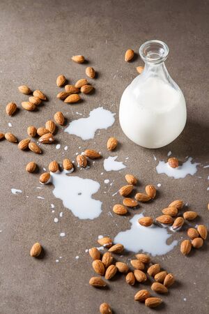 Dairy alternative milk. Almond milk in a glass bottle and fresh nuts over a gray background, selective focus. Clean eating, dairy-free, vegan, vegetarian, allergy-friendly, healthy food concept.の写真素材