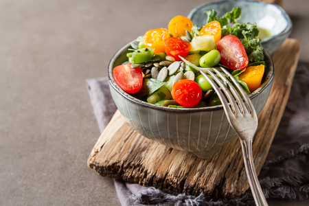 Green salad with tomatoes, spinach, green beans, onion, seeds in a ceramic plate with sauce. Dark backgroundの写真素材