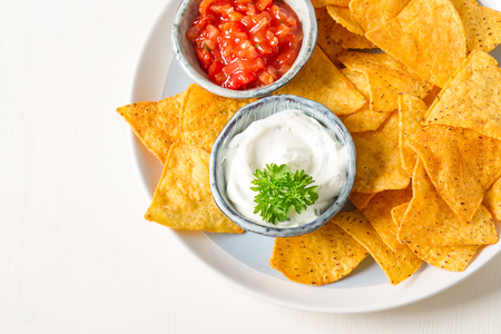 Snack for a party, chips with tortilla, nachos with sauces: salsa with tomatoes, sour cream. Mexican food. Bright white background. Top view. Copy space?の写真素材