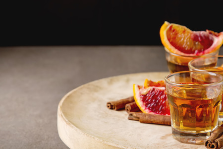 Golden tequila with red orange and cinnamon. Dark background. Selective focus.の写真素材