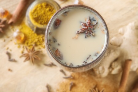 Traditional Indian masala tea in ceramic cup with spices to milk. Wooden batskgroundの写真素材