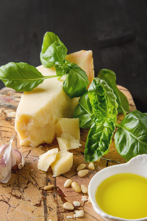 Italian parmesan cheese with knife fresh green basil,  oil, pine nuts and garlic. Ingredients for the pesto. Dark wood backgroundの写真素材