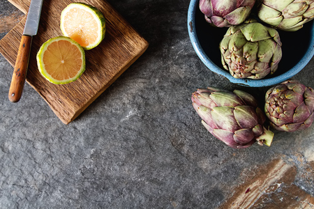 Baby ripping organic Artichokes with lemon. Food for a vegan and a vegetarian. Diet, food concept. Dark backgroundの写真素材