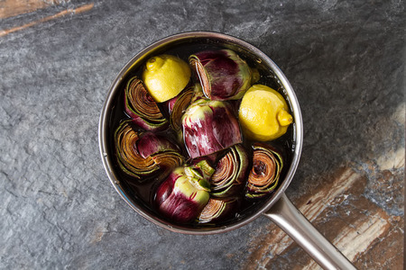 Baby ripping organic Artichokes with lemon. Food for a vegan and a vegetarian. Diet, food concept. Dark backgroundの写真素材