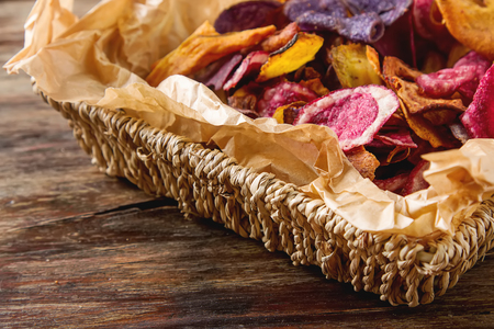 Beet and carrot salty chips on baking paper in an old brown wicker basket. Wooden  background.の写真素材