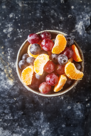 Plate with fruit salad of mandarin, grape, blueberry. Delicious and hearty breakfast options. Dark backgroundの写真素材