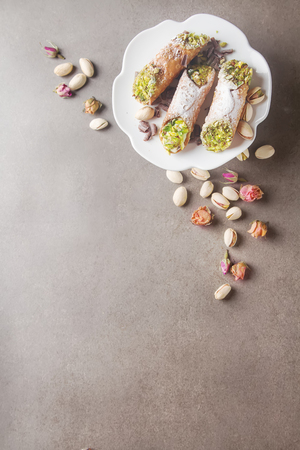 Sweet homemade cannoli stuffed with ricotta cheese cream and pistachios. Traditional Sicilian dessert. Italian pastry. selective focus. White cup of hot coffee. Dark backgroundの写真素材