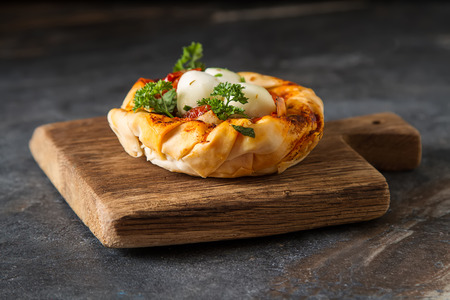Pie in the oriental style. Filo pastry with tomato and mozzarella. Dark background. Vegetarian food