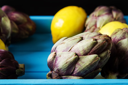 Baby ripping organic Artichokes with lemon. Food for a vegan and a vegetarian. Diet, food concept. Dark backgroundの写真素材