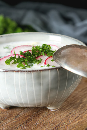 Summer cold soup - okroshka in a ceramic bowl. Ingredients of potatoes, radishes, cucumbers, parsley, eggs. Dark backgroundの写真素材