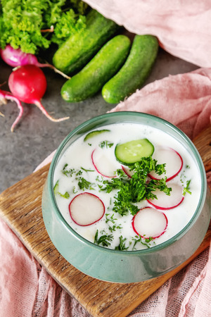 Summer cold soup - okroshka in a ceramic bowl. Ingredients of potatoes, radishes, cucumbers, parsley, eggs. Dark backgroundの写真素材
