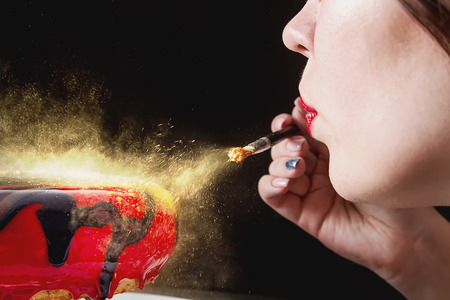 The process of preparing a mousse cake. Dark background. The girl is blowing gold on the cakeの写真素材