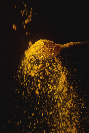 Metal spoon with yellow turmeric. Falling spices. Black backgroundの写真素材