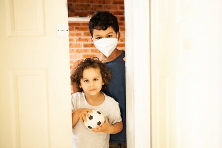 kids in self isolation during corona virus pandemic. Bored kids, sitting at home,  wearing a protective face maskの写真素材