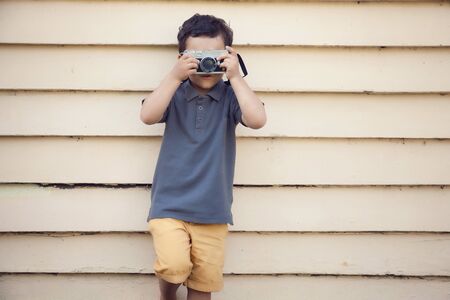 Young boy taking photo with camera, looking into the camera, sunshine, outdoorsの写真素材