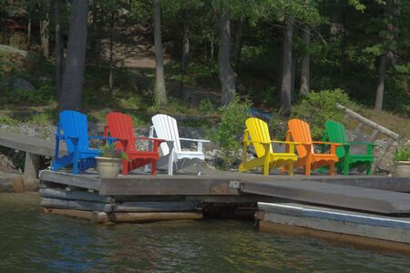 Six Chairs of different colours are resting on the deck and taking in the sunshineの写真素材