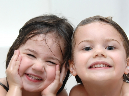Two sisters laugh through bath time with wet heads and smiles   Closeup shows one sister smiling and the other laughing の写真素材