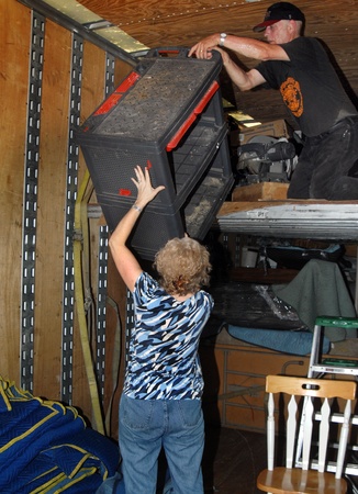 Couple work together to unload their moving van   Husband is handing tool box to wife standing on floor   It is hot work inside van の写真素材