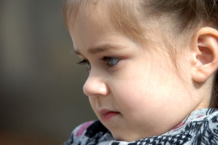 Lost in thought, this little girl is in profile and close up.  She is resting her chin on her chest.の写真素材