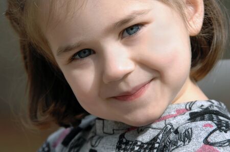 Adorable little girl beams at the camera.  Closeup photo with light sparkling from her eyes.