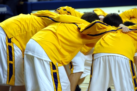High school varsity basketball team huddles together before game start.  Uniforms are yellow, purple and white.の写真素材