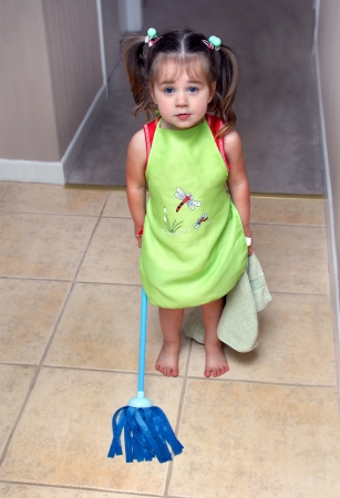 All hands on deck!  This little girl is ready and willing to help her mother with household chores.  She is wearing her apron, holding her dusting rag and weilding her mop.の写真素材