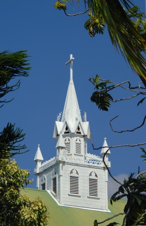 St. Benedict Roman Catholic Church on the Big Island of Hawaii, has an elaborate and oranate belfry.  White, wooden and ornate, the steeple of this church is framed by vivid blue sky.の写真素材