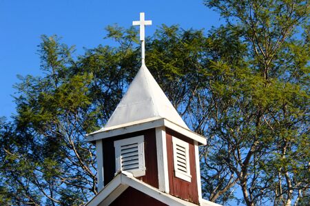 Quaint red, wooden church on the Big Island of Hawii has battered tin roof, cracked, painted wood and a metal cross topper.の写真素材