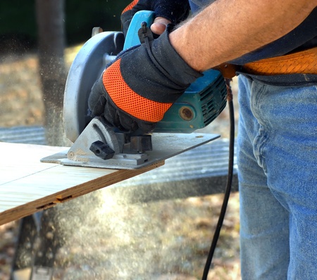 Man holds circular saw and cuts plywood on construction site.  Shot shows hands and tool and saw dust flying.のeditorial素材