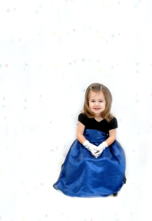 Little girl is wearing a royal blue gauze dress with velvet bodice.  She has long hair and is seated in front of a flower print curtain.の写真素材