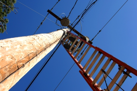 Unusual view of telephone repairman working at the top of a 30 foot ladder.  Sky is vivid blue.の写真素材