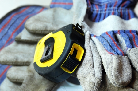 Bright yellow tape measure lays across a pair of dirty work gloves.の写真素材