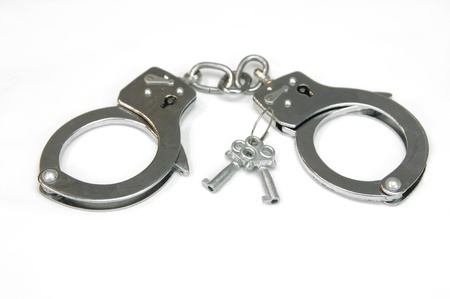 Pair of silver handcuffs lay besides two keys that can unlock them.  Cuffs lay on all white surface.の写真素材