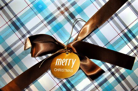Turquoise and brown plaid wrapping paper covers Christmas gift.  Brown ribbon and gold tag tie up package.の写真素材