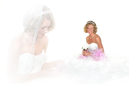 Young bride smiles happily as she sits in an all white room.  She has pink boa feathers draped around her shoulders and is holding a small poesy of white roses.の写真素材