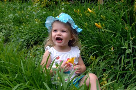 Small child yells as a yellow spring flower showers her nose with yellow pollen.  She is wearing a turquoise and white dotted hat.の写真素材
