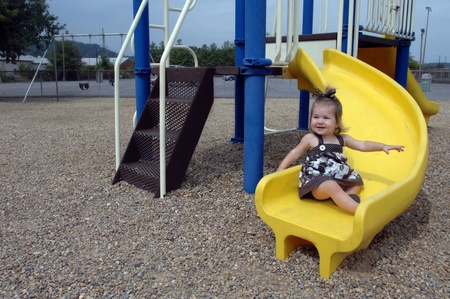 Little girl takes a turn on a yellow slide all by herself   She is smilng in pleasure with arms extended for balance の写真素材