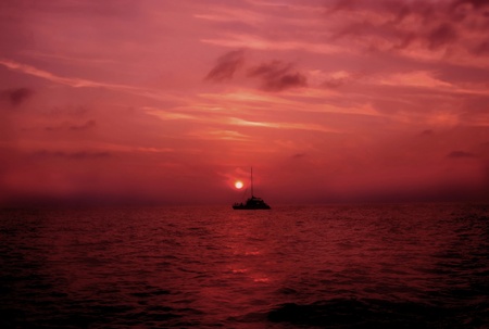Boat sails across the reflection of a red sun at sunset    Solitary boat on a vast ocean of color の写真素材
