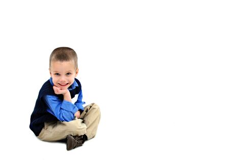Little boy sits in an all white room   He is dressed in khakis and a navy sweater vest   He is grinning from ear to ear の写真素材