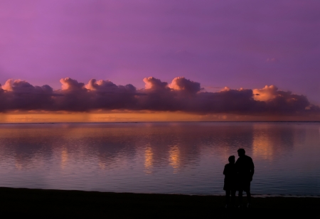 Older couple still in love and enjoying a sunset together, stand on the shores of Kauai, Hawaii and look into each otherの写真素材