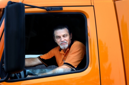 Big rig driver looks out the window of his orange truck while making a delivery   He is wearing...