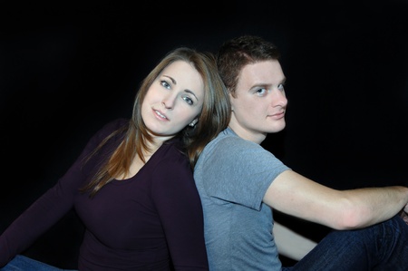 Black background frames young couple   Both are unsmiling and somber   They are dressed casual in jeans の写真素材