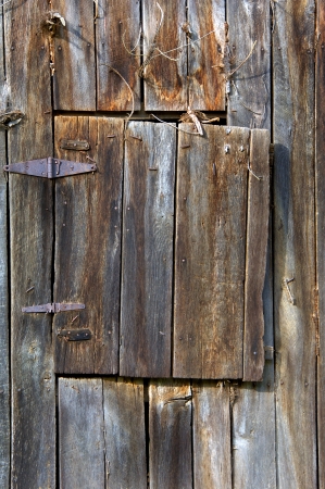 Weathered wood, leather and iron hinges hold an aging loft door to this old barn covered with rusty and bent nails の写真素材